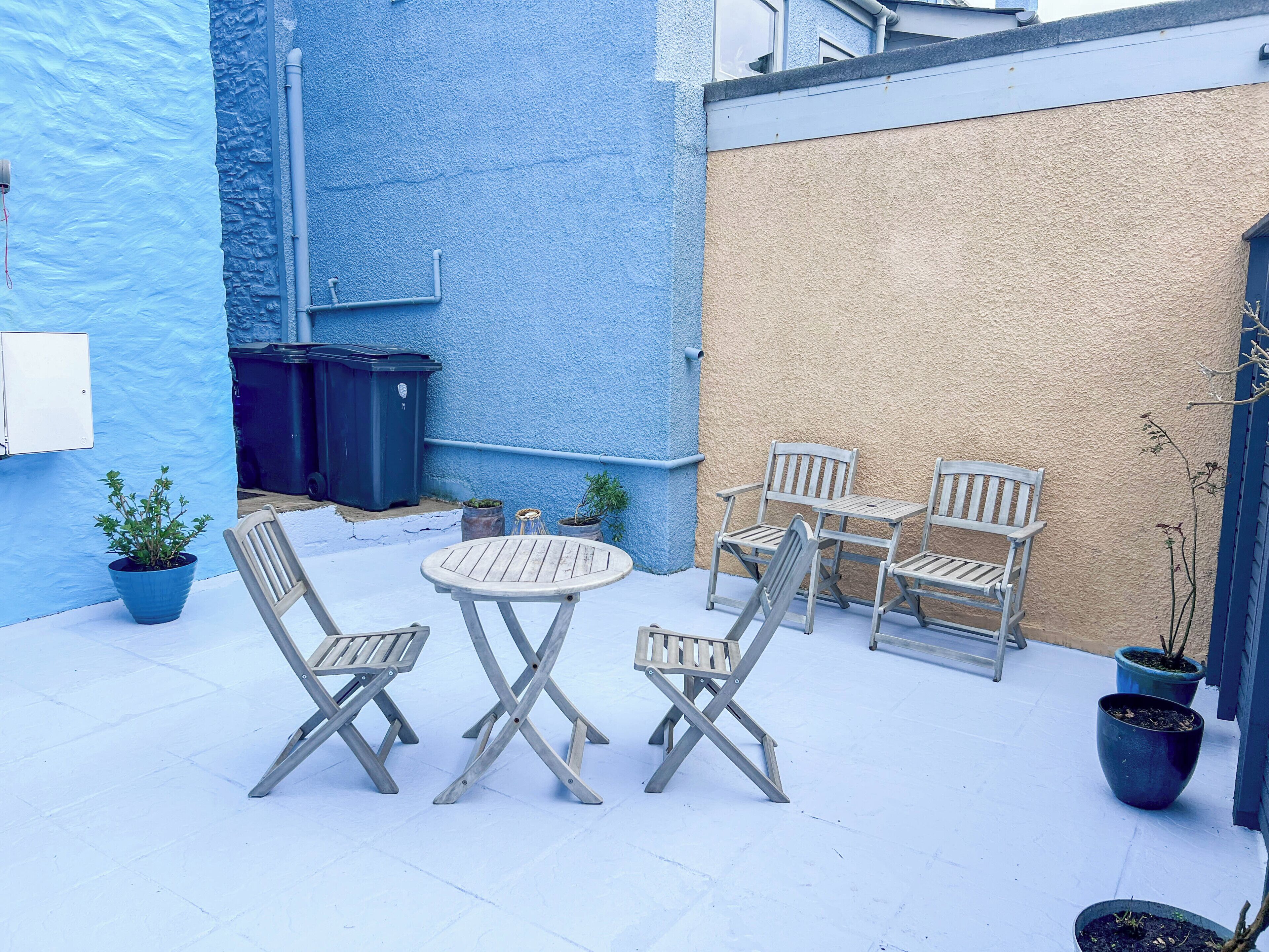 A patio with a table and four chairs, potted plants, and a blue and beige wall.