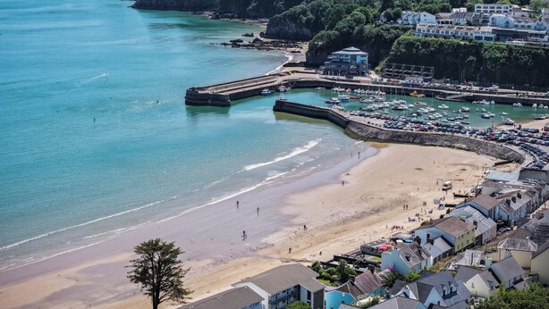 Une ville côtière dotée d’une plage de sable, d’un port de plaisance avec des bateaux et d’immeubles résidentiels.