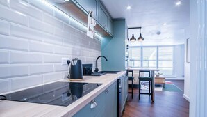 Une cuisine moderne dotée d’une plaque de cuisson à induction noire, de meubles de couleur turquoise et d’une fenêtre donnant sur un coin repas.