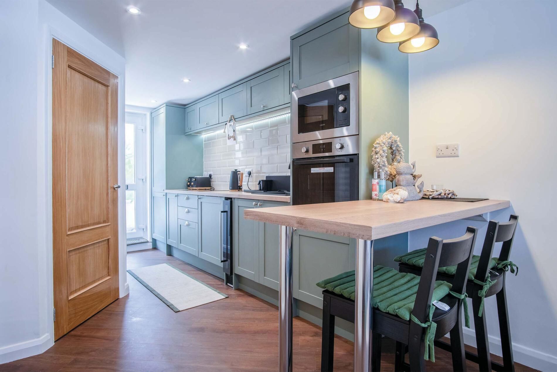 Eine moderne Küche mit hellblauen Schränken, einem Edelstahlbackofen und einem Holzespeisetisch mit Stühlen.