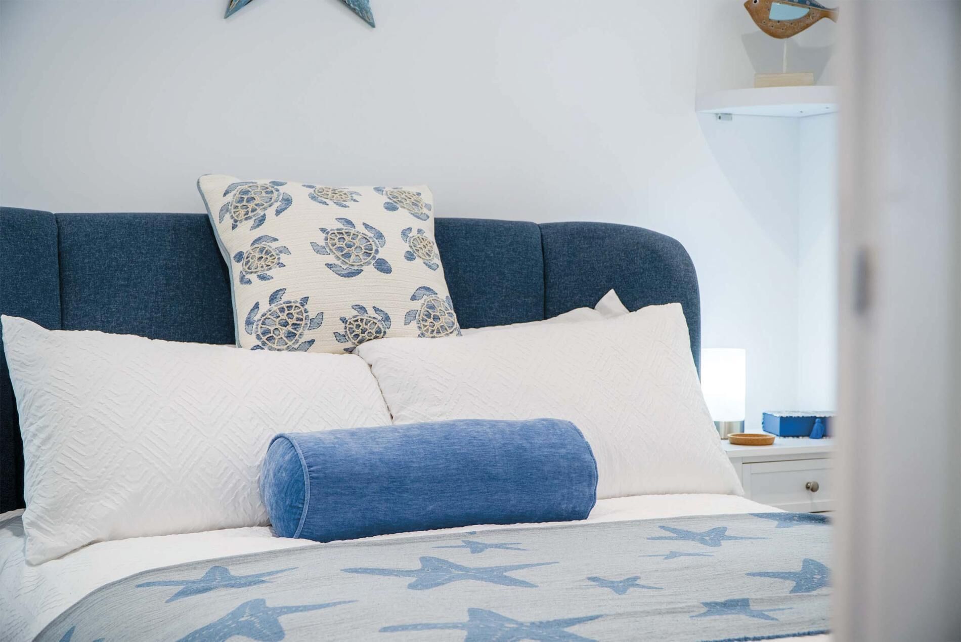 A bed with a blue headboard, white and blue pillows, and a blue blanket with star patterns.