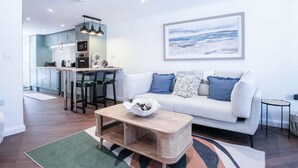 Un salon moderne avec un canapé blanc, une table basse et une cuisine en arrière-plan.