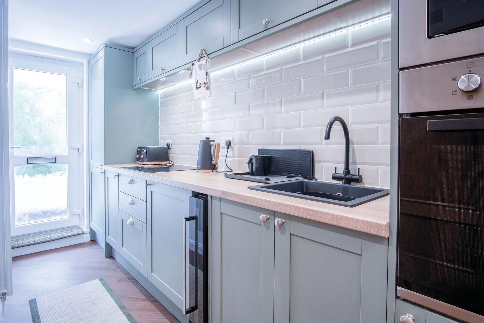 A modern kitchen with grey cabinets, a black countertop, a sink, a toaster, a kettle, and a built-in oven.
