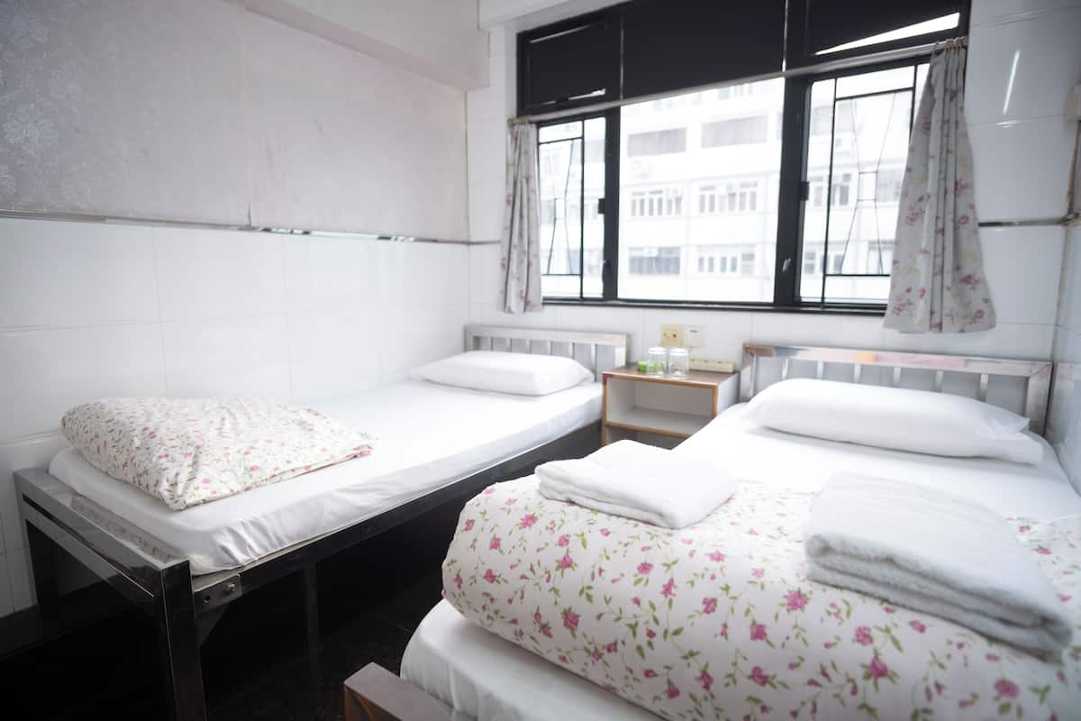 A twin room with two beds, a window with curtains, a small bedside table, and a radiator.