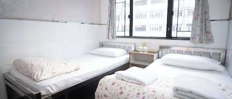 A twin room with two beds, a window with curtains, a small bedside table, and a radiator.