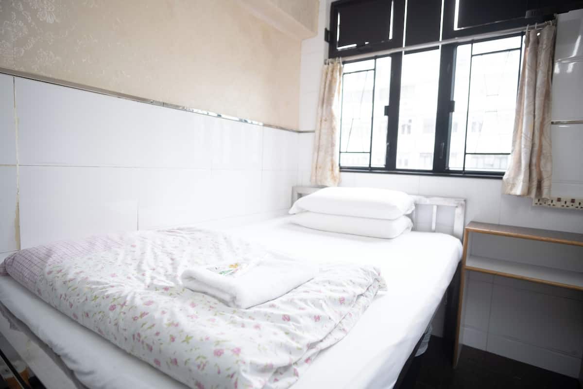A neatly made bed with floral bedding, a bedside table, and a window with curtains.