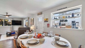 A dining area with a round table set for four, a coffee bar with various mugs and a coffee machine, and a television mounted on the wall. - Spacious Retreat with Hot Tub, Patio, & King Bed (Olympia)