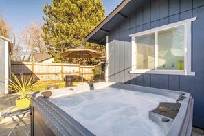 Een jacuzzi in een achtertuin met een houten omheining, een plant in een pot en een raam.