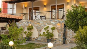 A two-story building with a balcony, stone arches, and potted plants.