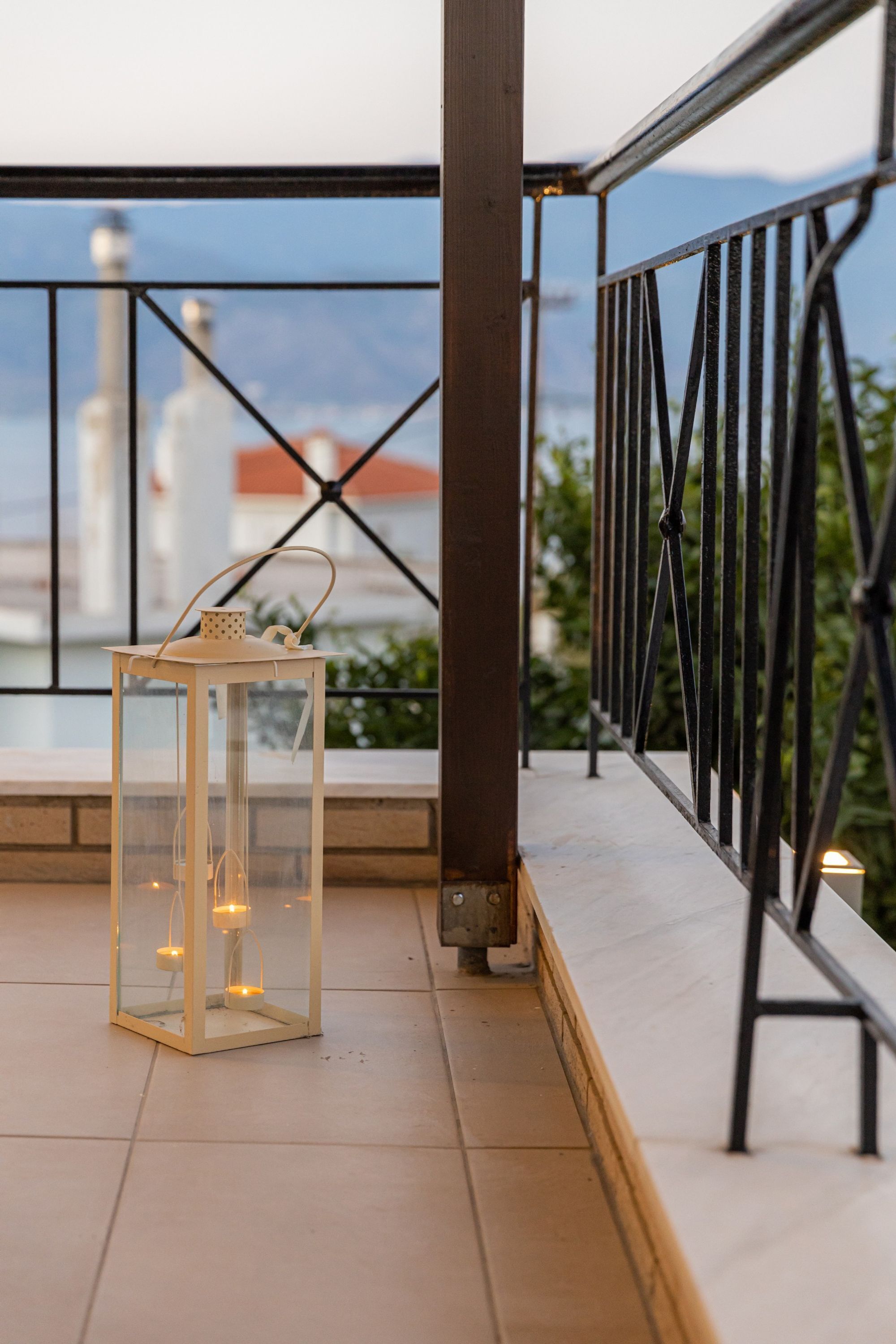 A balcony with a glass lantern table, metal railing, and a view of distant buildings.