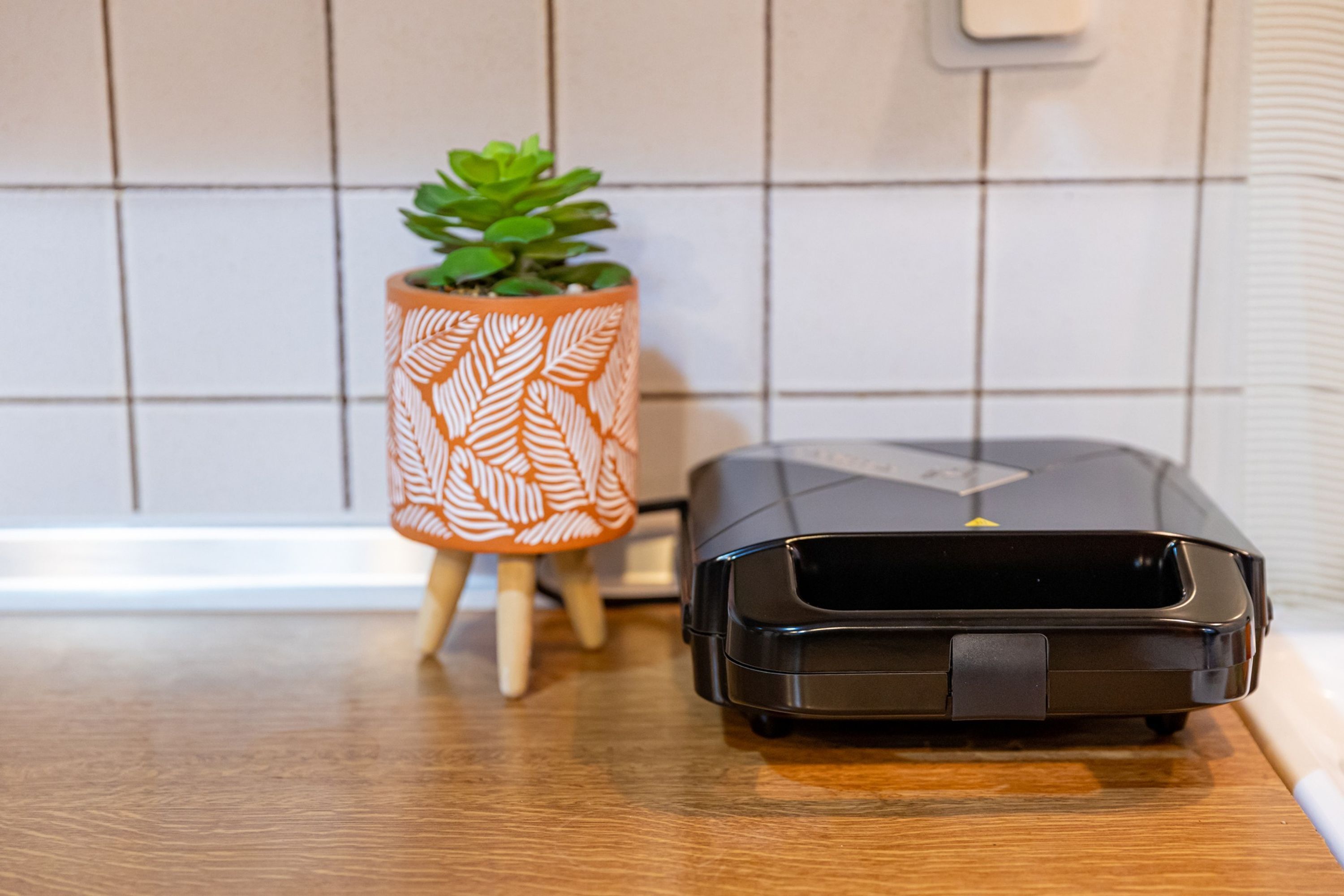 A portable printer on a wooden surface next to a potted plant with a leaf pattern.