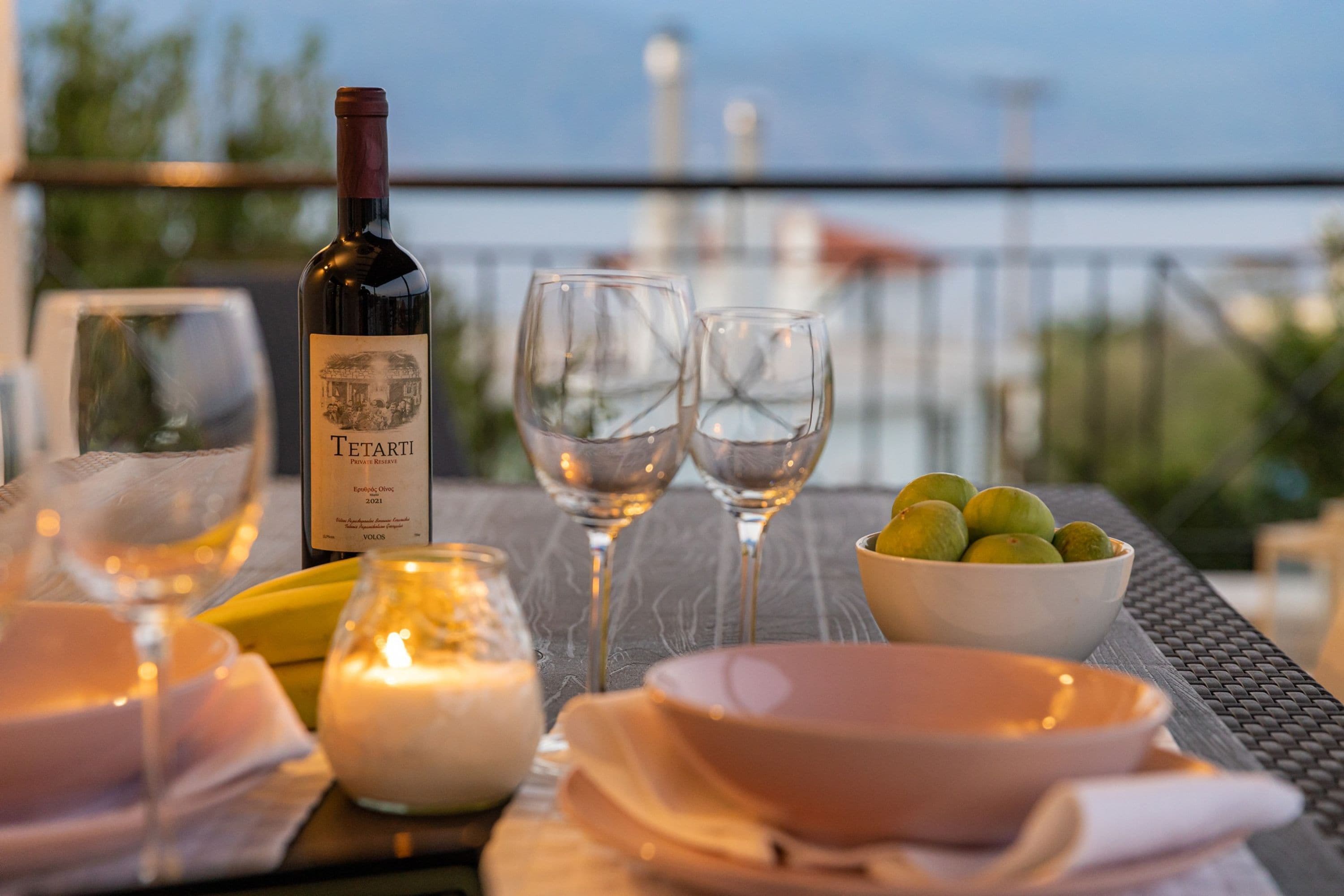 A table set for two with a bottle of wine, glasses, a bowl of fruit, and candles.