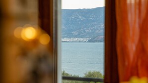 A view through a window with a curtain, overlooking a body of water and distant land.