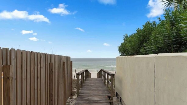 En træpromenade der fører til en strand med kig til havet.