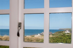A view through a window with a coastal landscape, including houses and the sea. - No. 9 The Dairy: A beachside barn conversion on Anglesey (Llanfaethlu)