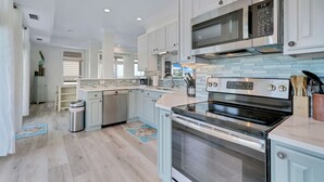 Une cuisine moderne avec des meubles blancs, des appareils en acier inoxydable et un pare-feu bleu clair.