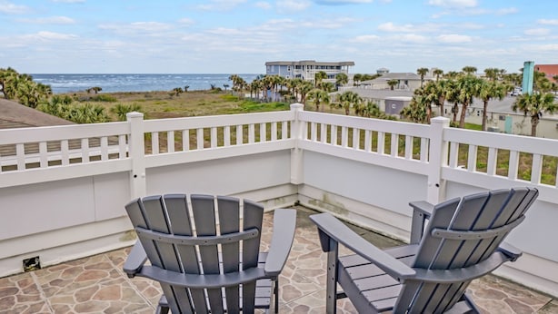 Un balcon avec deux fauteuils Adirondack, une clôture blanche et une vue sur l’océan et la plage.