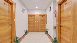 A hallway with wooden doors, potted plants, and a fire extinguisher on the wall. - Hotel Rush Imperial (Indore)