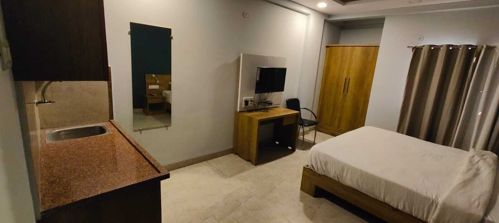 Un dormitorio con cama, escritorio con computadora, armario y baño con lavamanos.