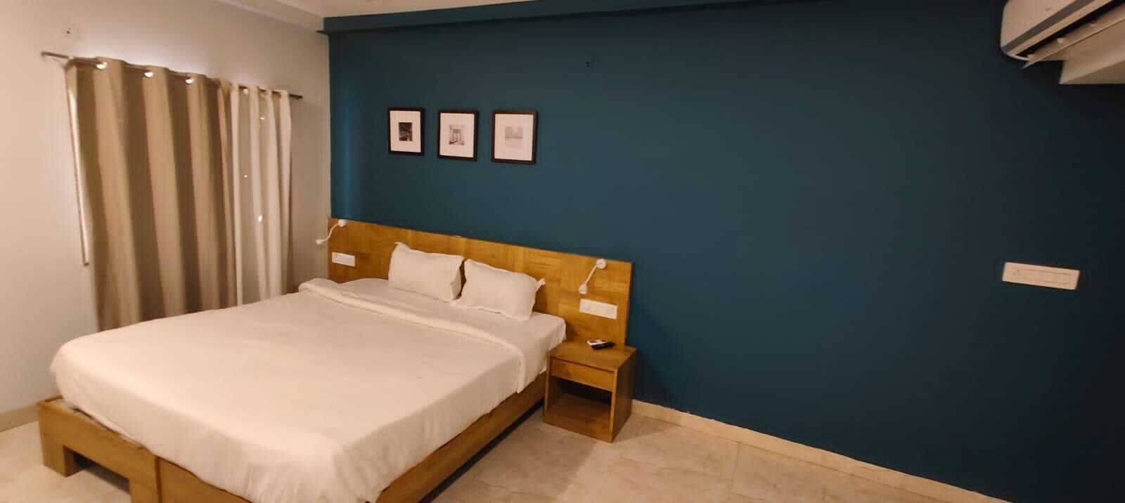A bedroom with a bed, wooden headboard, bedside table, and a wall with three framed pictures.