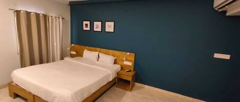 A bedroom with a bed, wooden headboard, bedside table, and a wall with three framed pictures.