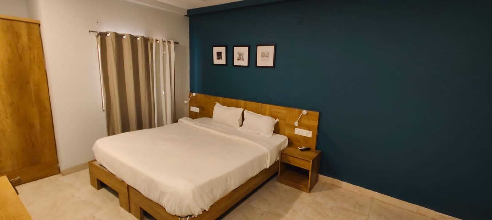 Un dormitorio con una cama de madera, una mesita de noche, una cortina y tres cuadros en la pared.