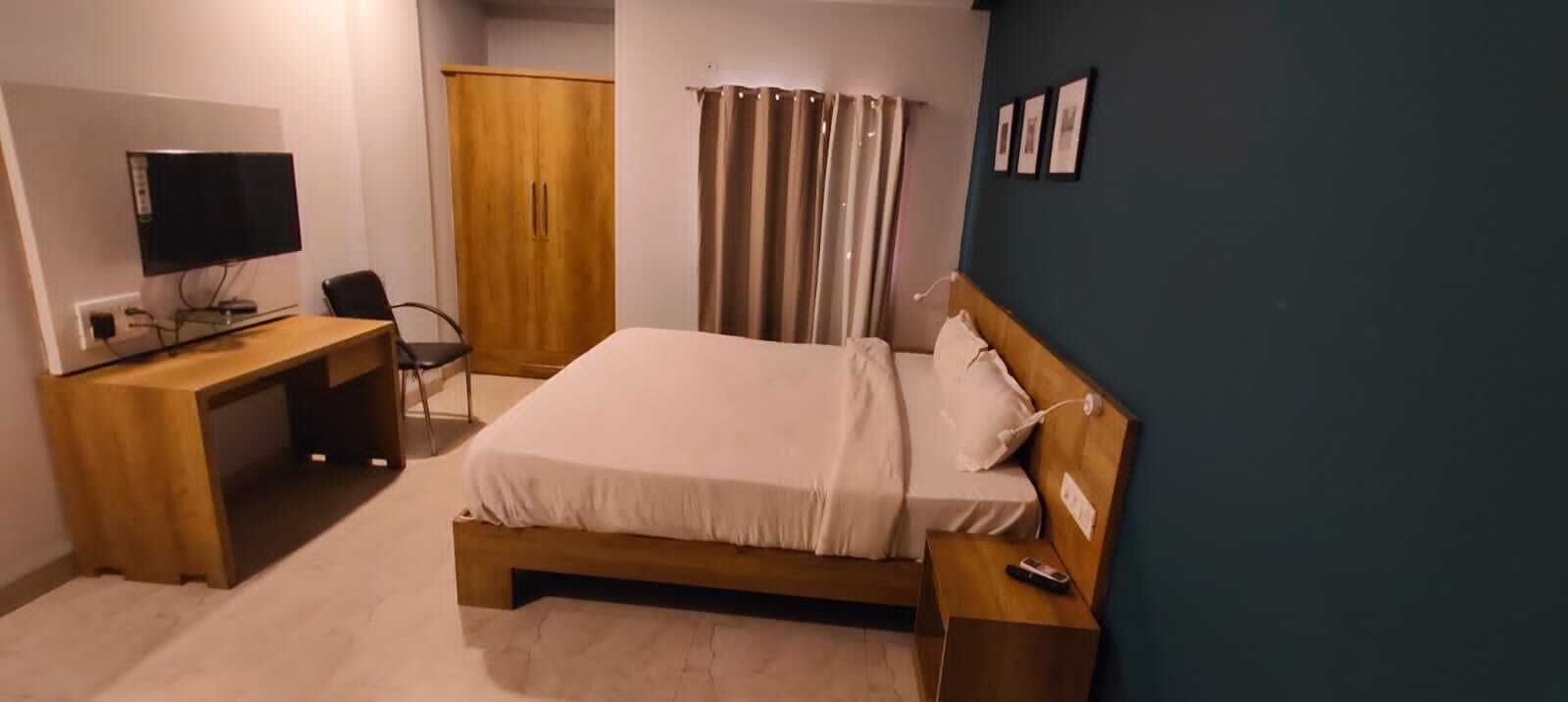 A bedroom with a bed, a desk with a computer, a wardrobe, and a TV.