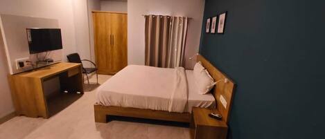 A bedroom with a bed, a desk with a computer, a wardrobe, and a TV.