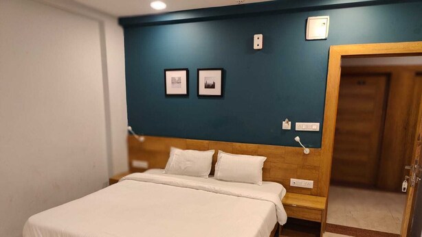 A neatly made bed in a room with a wooden headboard, a blue accent wall, and two framed pictures. - Hotel Rush Imperial (Indore)
