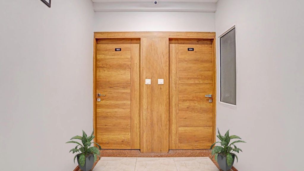 A hallway with two wooden doors, each marked with a number. There are potted plants at the entrance.