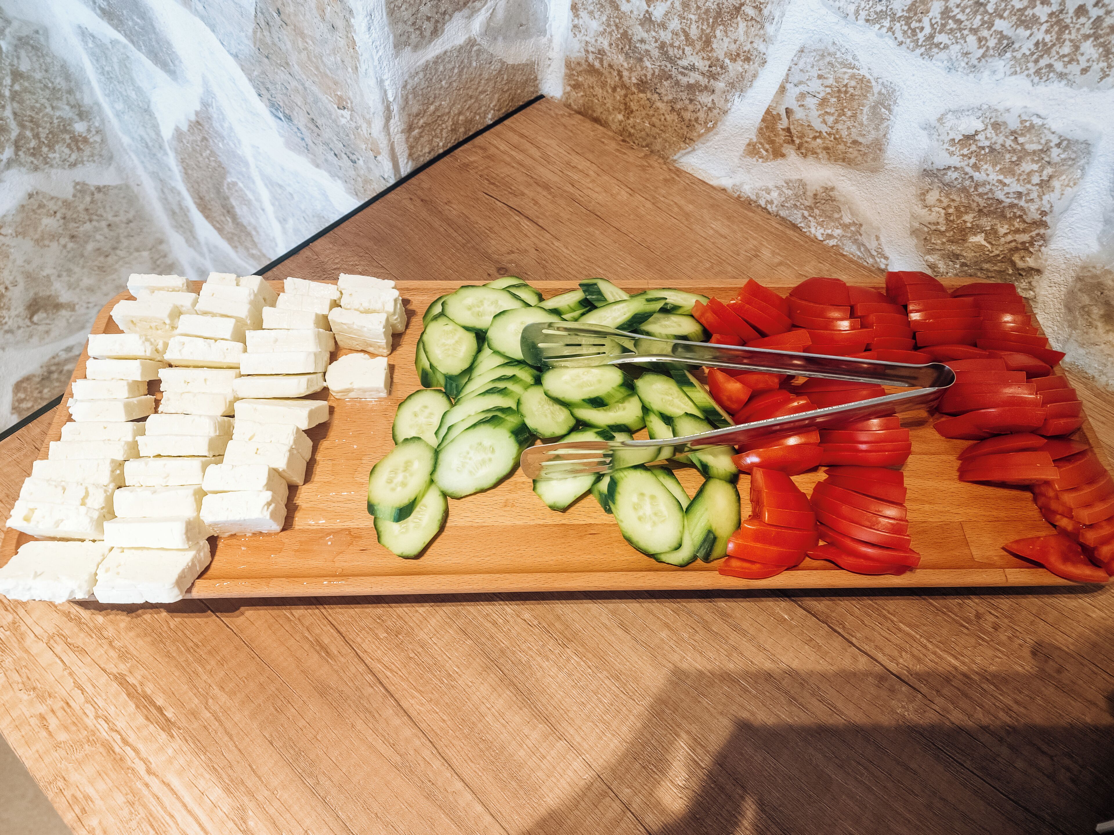 A wooden cutting board with cheese, cucumbers, and tomatoes.