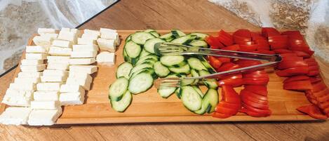 A wooden cutting board with cheese, cucumbers, and tomatoes.