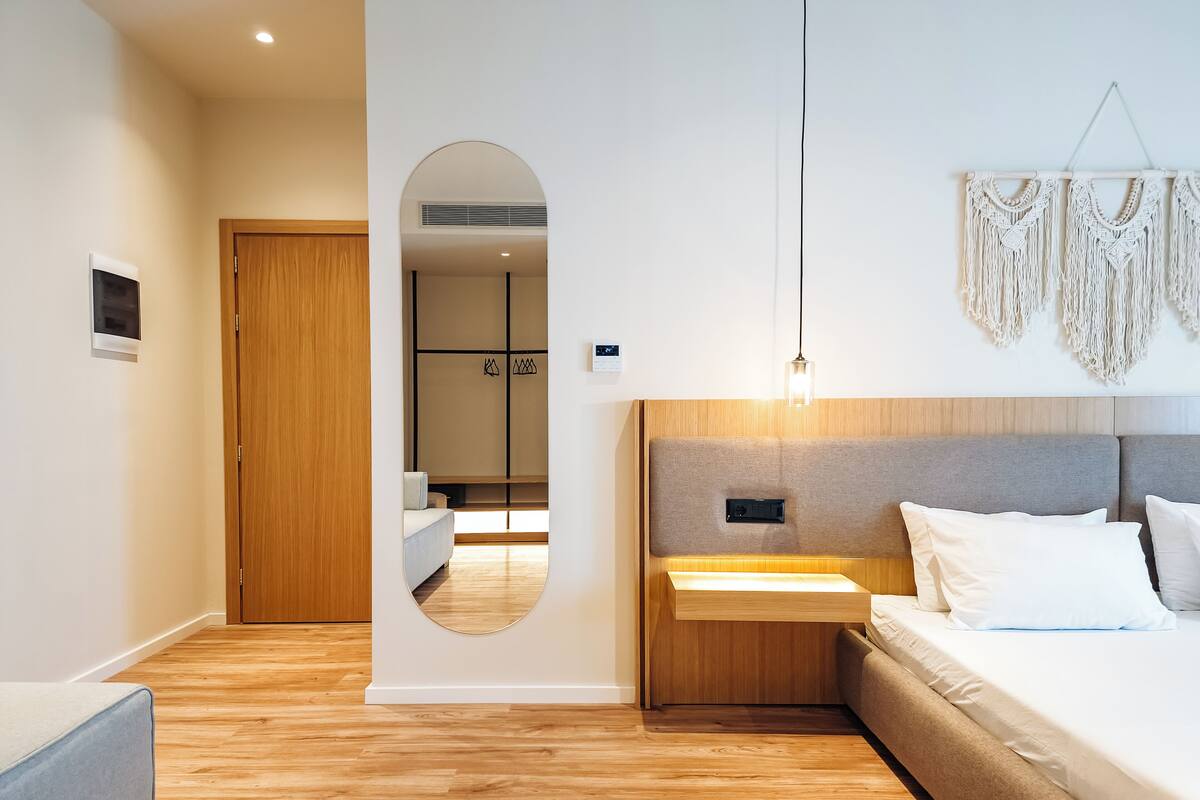 A modern bedroom with a wooden floor, a bed with white bedding, a bedside table, and a wall-mounted macrame decoration.