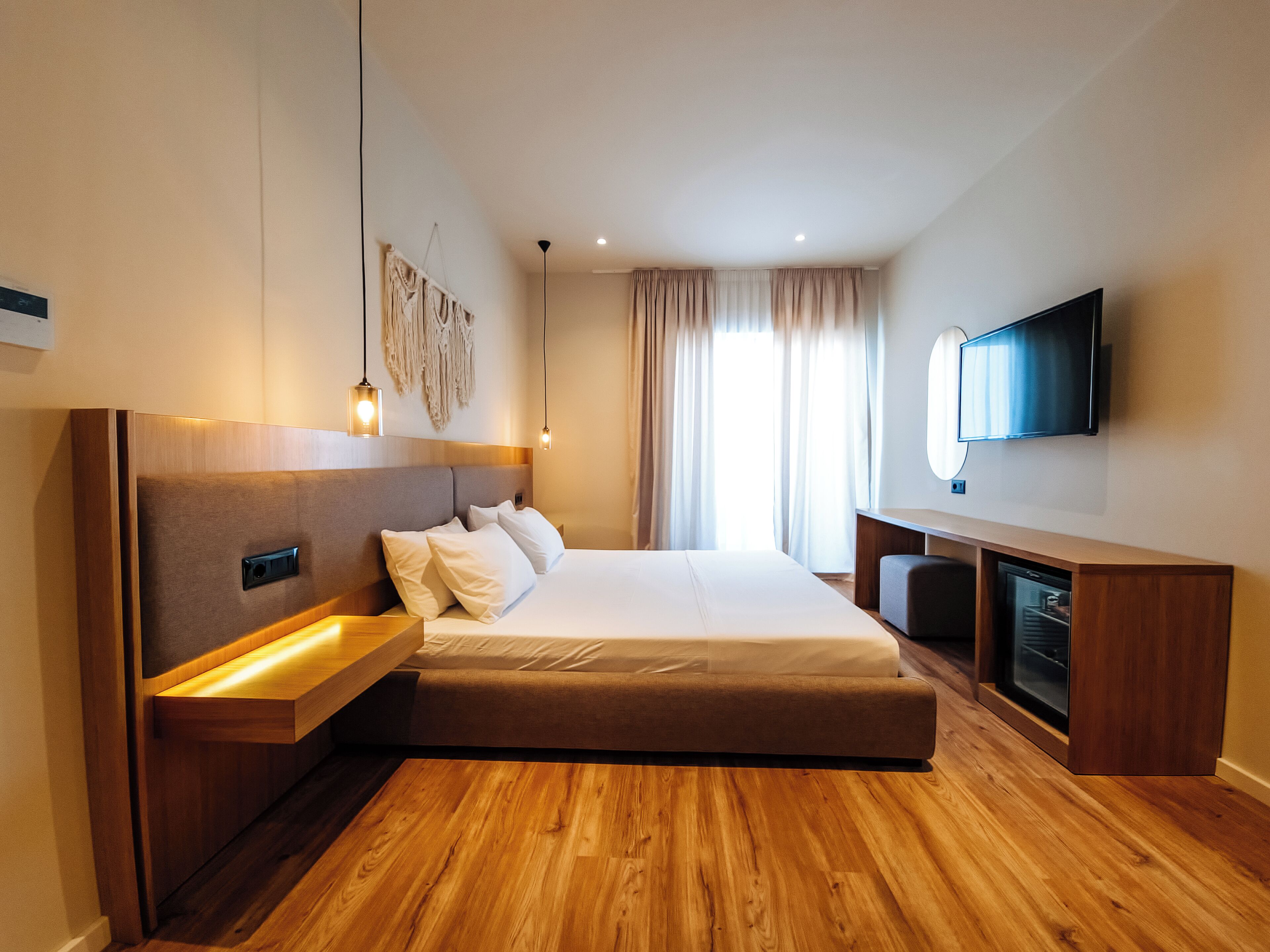 A modern hotel room with a large bed, wooden flooring, a flat-screen TV, and a built-in entertainment unit.
