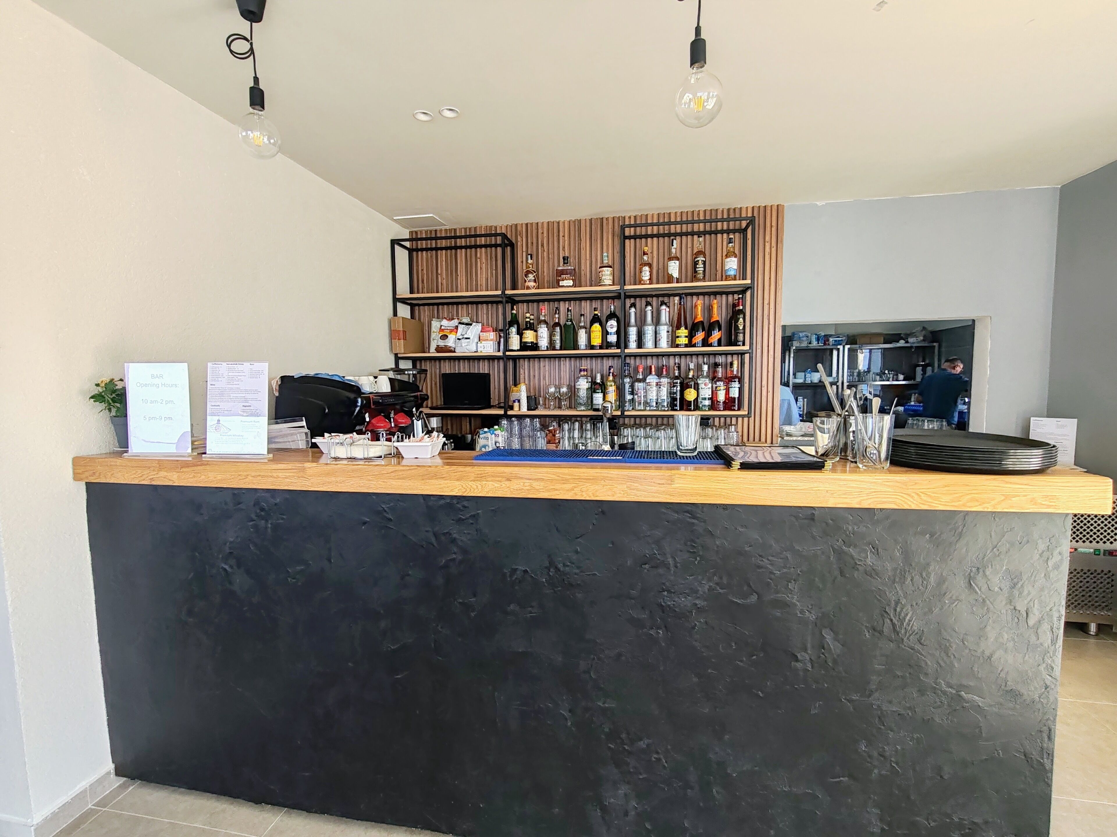 A bar area with a wooden counter, shelves stocked with bottles, and a coffee machine.