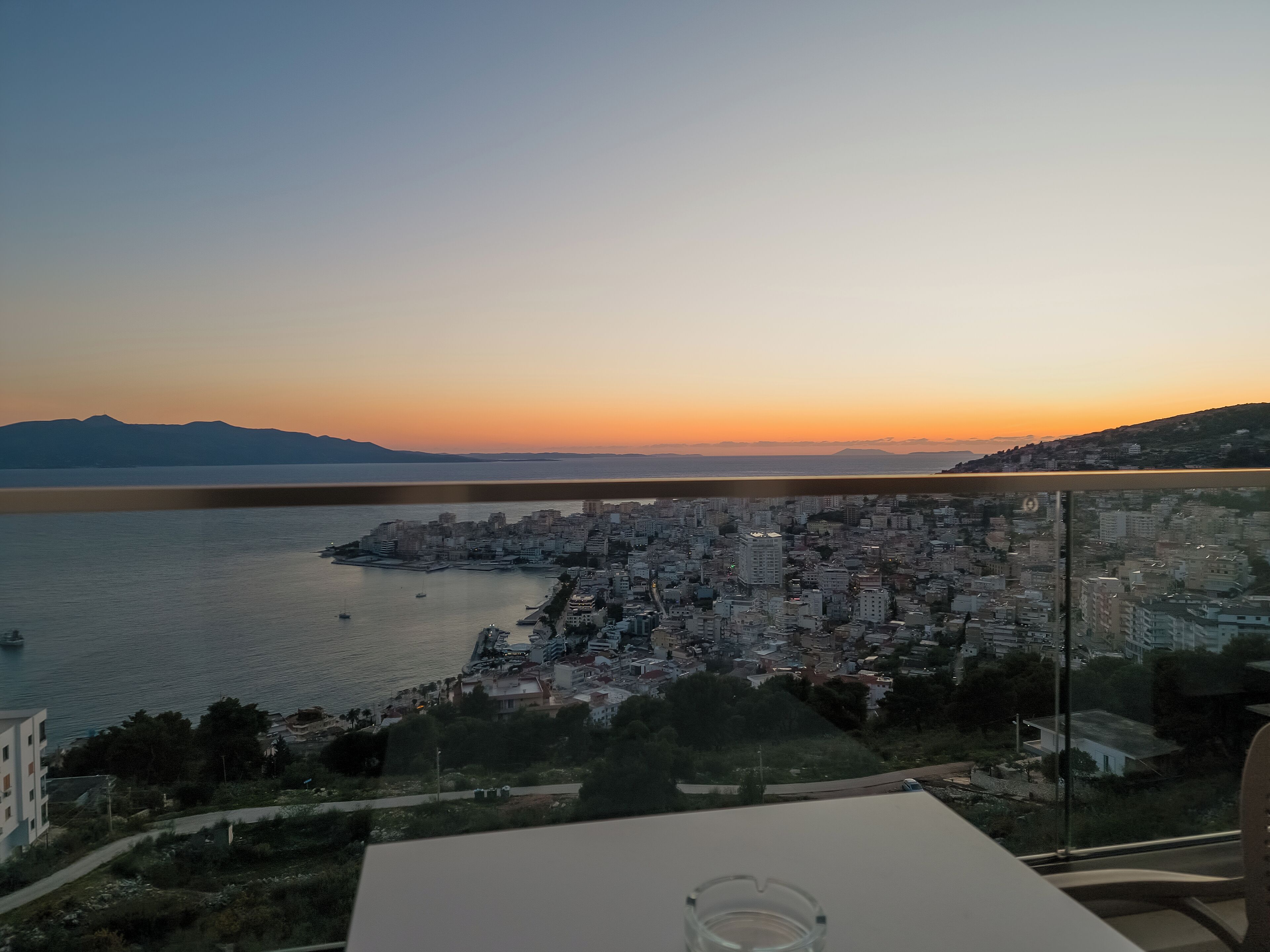 A cityscape with a view of a body of water and distant mountains during sunset.