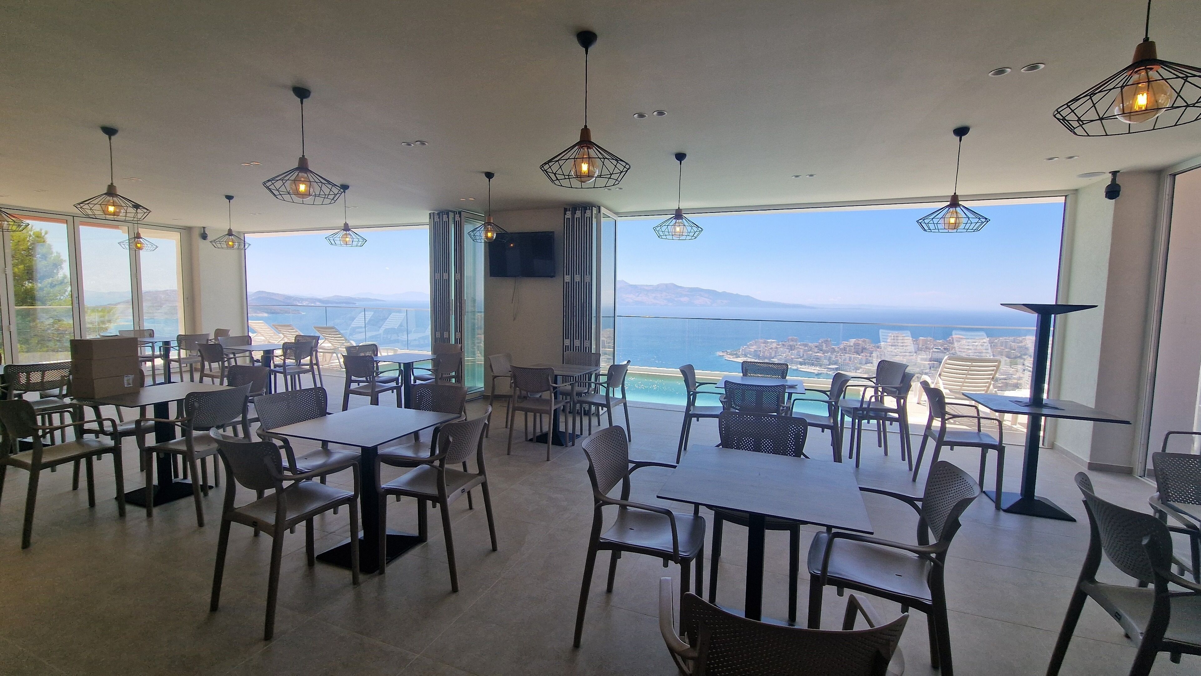 Un restaurante con mesas y sillas, ventanas amplias y lámparas colgantes.