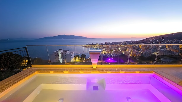 A rooftop pool with a city view, a glass railing, and a sunset in the background. - Sunset Shoreline Saranda Hotel (Sarandë)