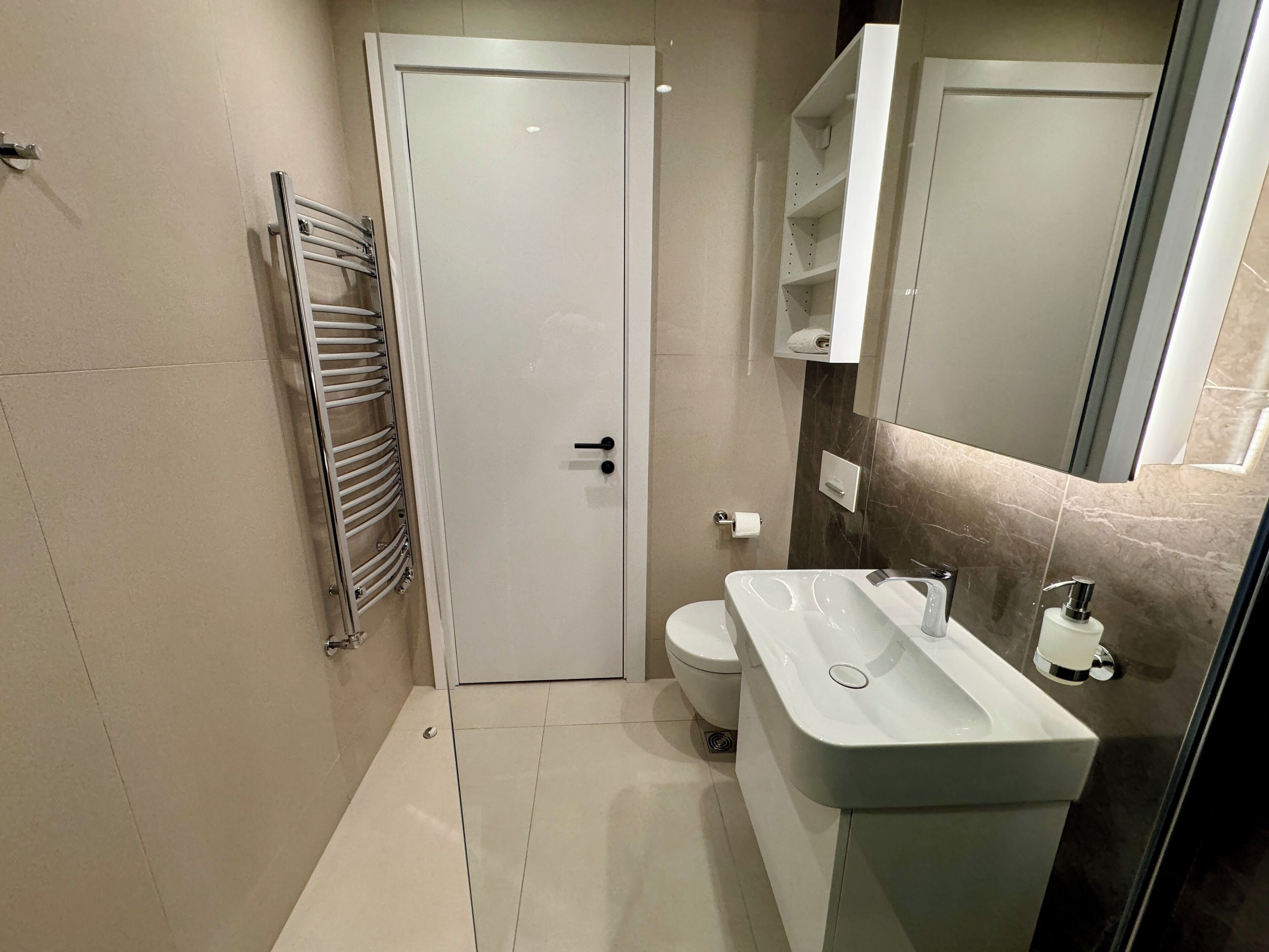 A modern bathroom with a white door, a towel rack, a toilet, and a sink with a mirror above it.