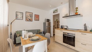 Eine moderne Küche mit Essbereich, ausgestattet mit einem Holztisch, weißen Stühlen, einem eingebauten Backofen und einem Kühlschrank.