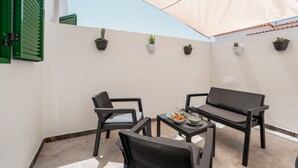 Eine Terrasse mit Tisch und Stühlen, ein kleiner Tisch mit einer Schüssel Essen und Blumentöpfe an der Wand.
