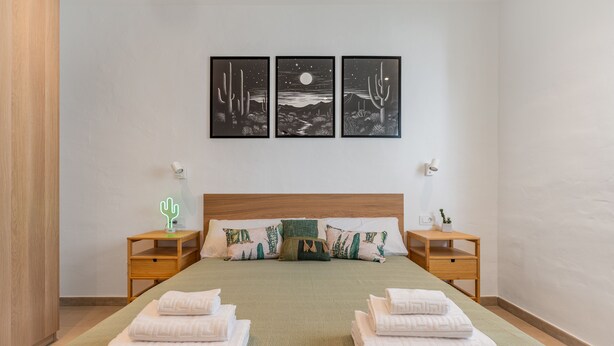 Ein ordentlich gemachtes Bett mit zwei Kissen, ein Nachttisch mit Lampe und eine Wand mit drei gerahmten Bildern.