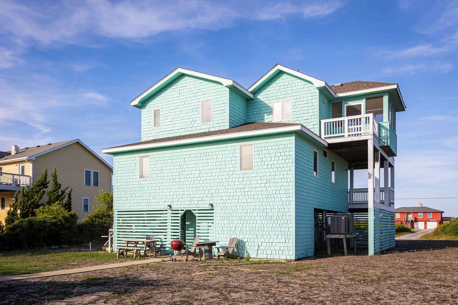 A two-story building with a light blue exterior, a balcony on the upper floor, and a small front porch with outdoor seating.