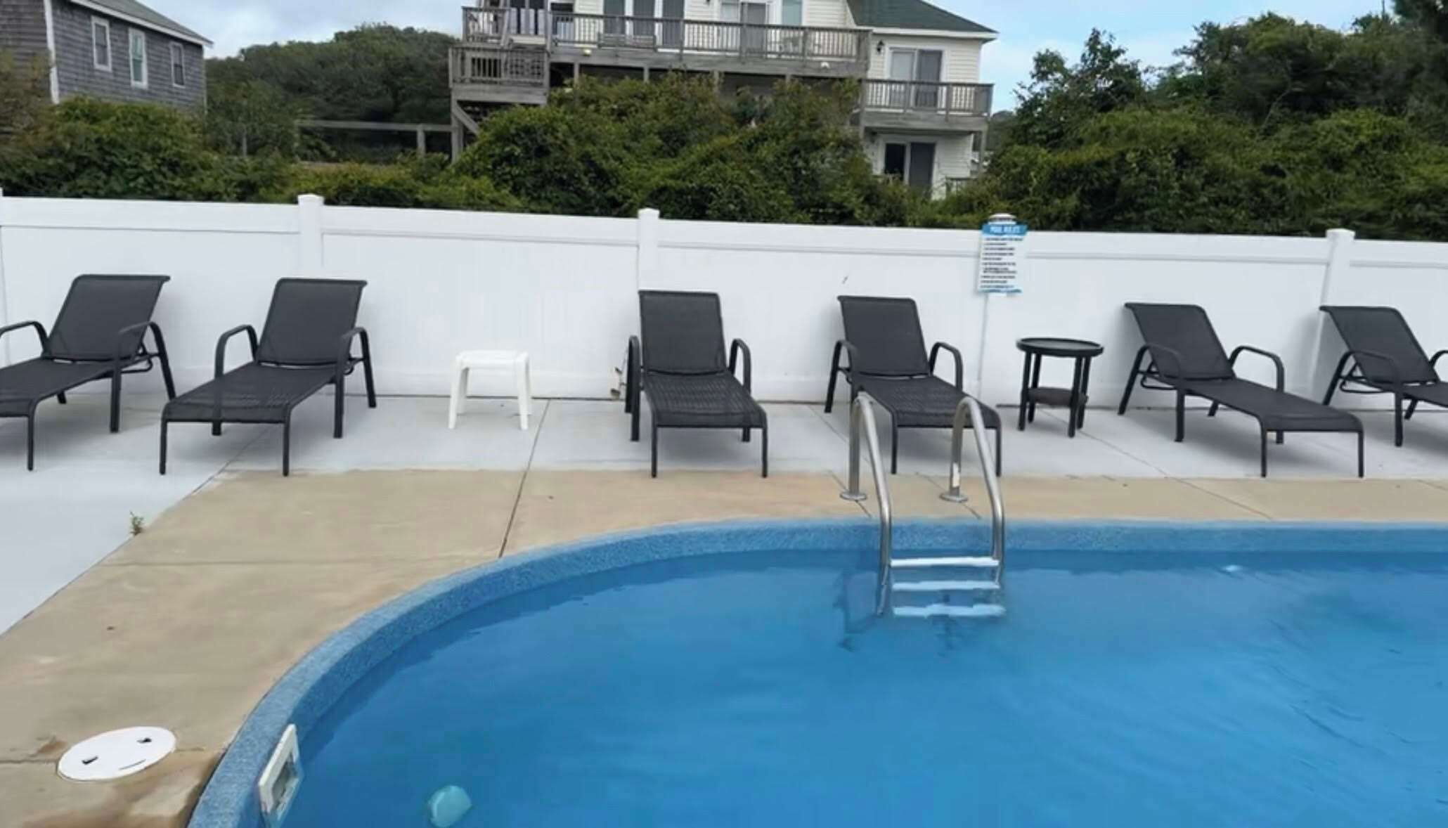 A swimming pool with lounge chairs and a small white table.