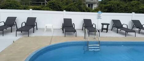 A swimming pool with lounge chairs and a small white table.