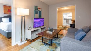 Een moderne woonkamer met een flatscreen-tv, een houten salontafel, een grijze bank en een vloerlamp.