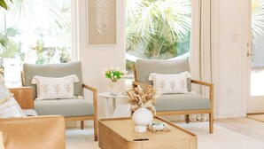 A modern living room with two grey armchairs, a wooden coffee table, and a small white side table with a vase of dried flowers. - St. Augustine 3BR Retreat · 2 King Suites · Putting Green · 1 Mi. to Downtown (St. Augustine)