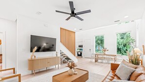 A modern living room with a flat-screen TV, a wooden coffee table, a leather sofa, and a dining area with a table and chairs. - St. Augustine 3BR Retreat · 2 King Suites · Putting Green · 1 Mi. to Downtown (St. Augustine)