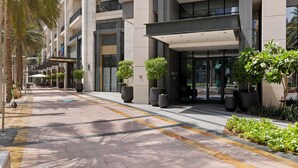 Entrada d'un hotel modern amb una passera coberta, plantes grans en testos i un sòl net revestit de rajoles.