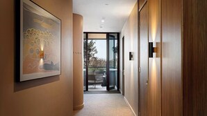 Un couloir orné d’un tableau abstrait encadré, avec une porte en bois et une vue sur un espace extérieur aménagé avec des tables et des chaises, visible à travers des portes vitrées.